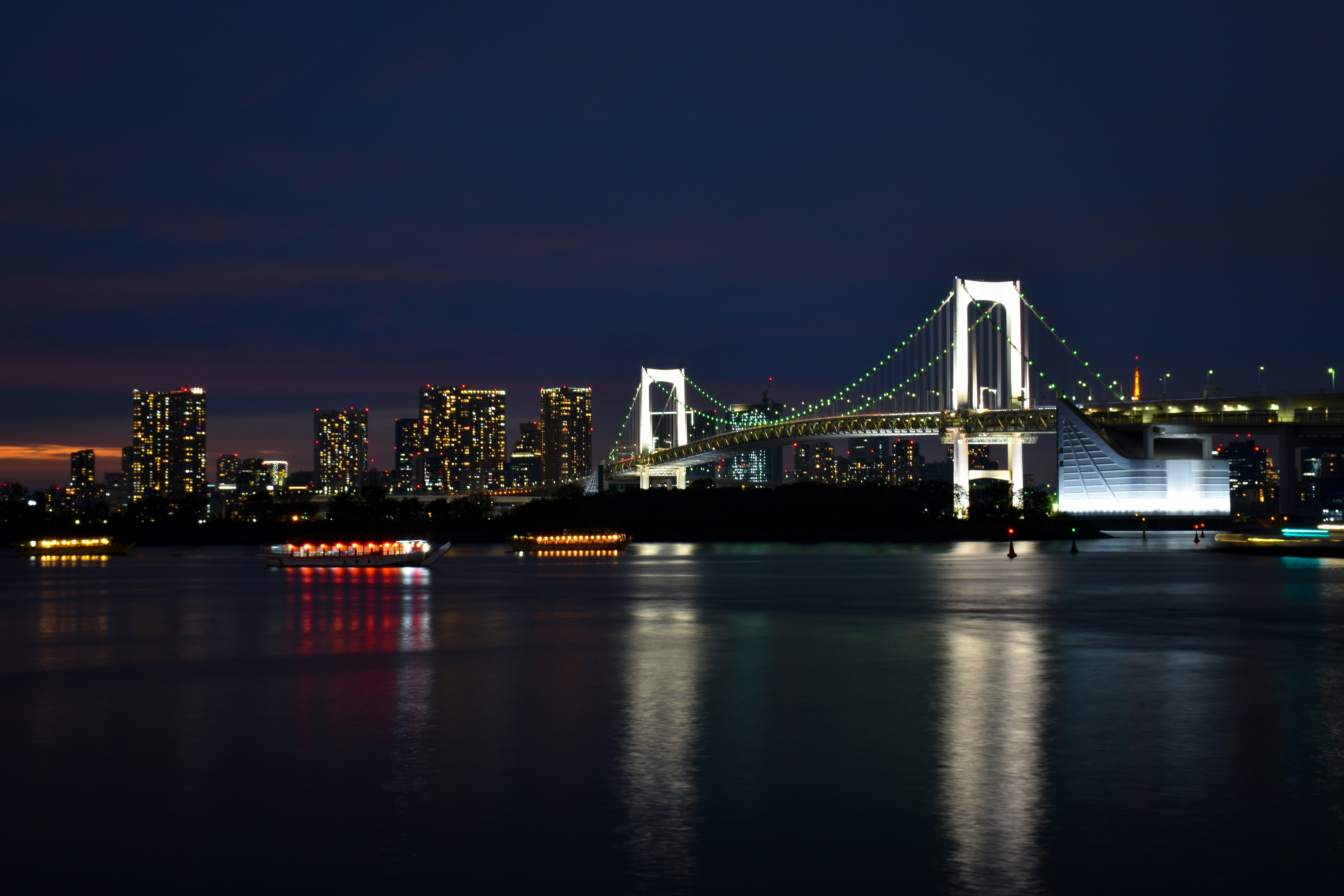 Rainbow Bridge spanning Tokyo Bay at sunset with orange and purple sky from Odaiba