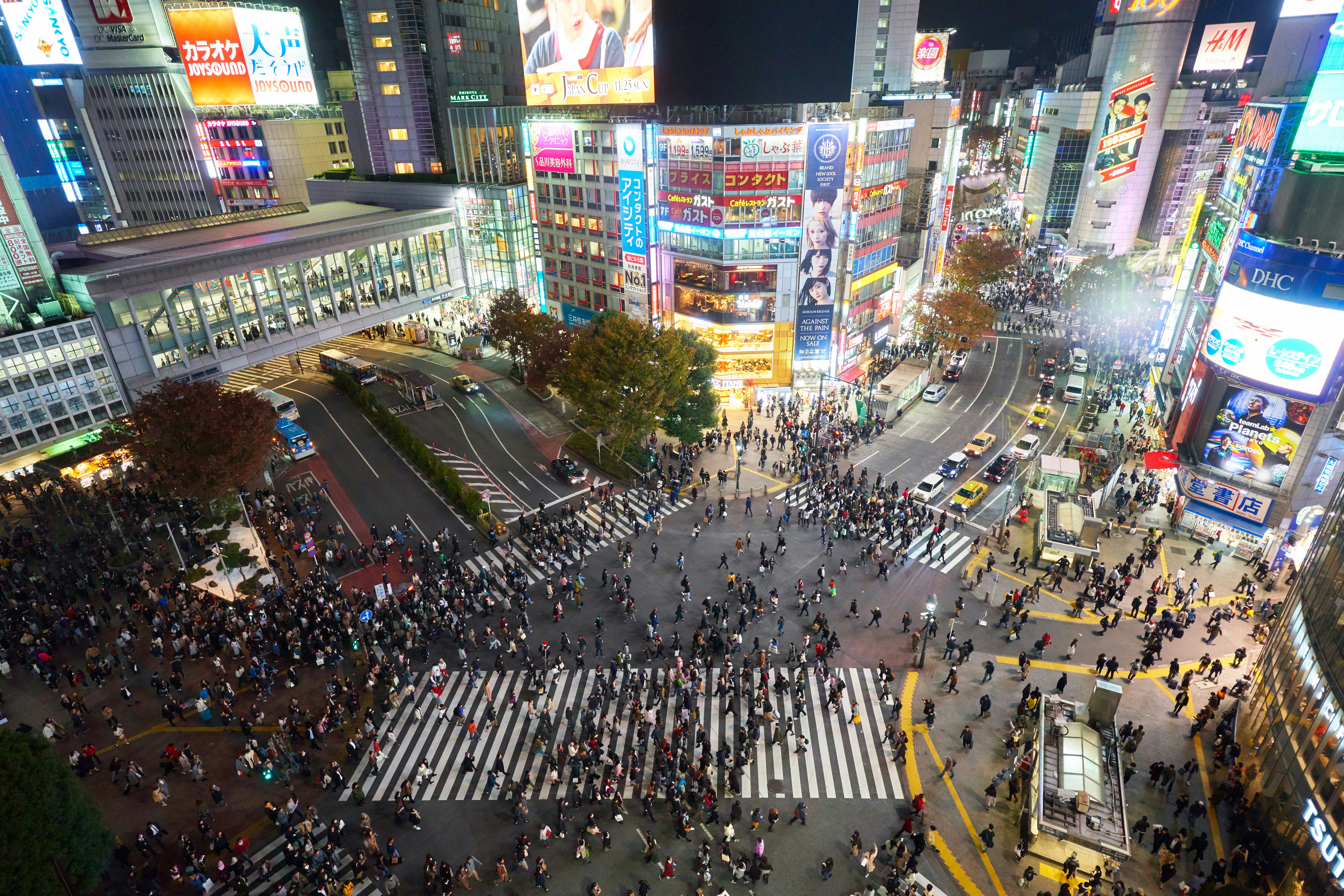 Shibuya Crossing at night with crowds under bright neon lights and advertising screens